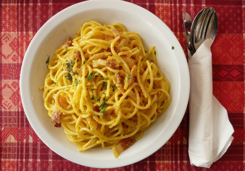 piatto di carbonara su un tavolo con forchetta e cucchiaio