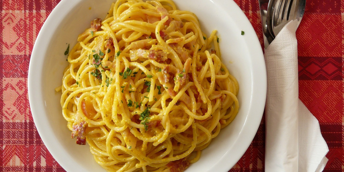 piatto di carbonara su un tavolo con forchetta e cucchiaio